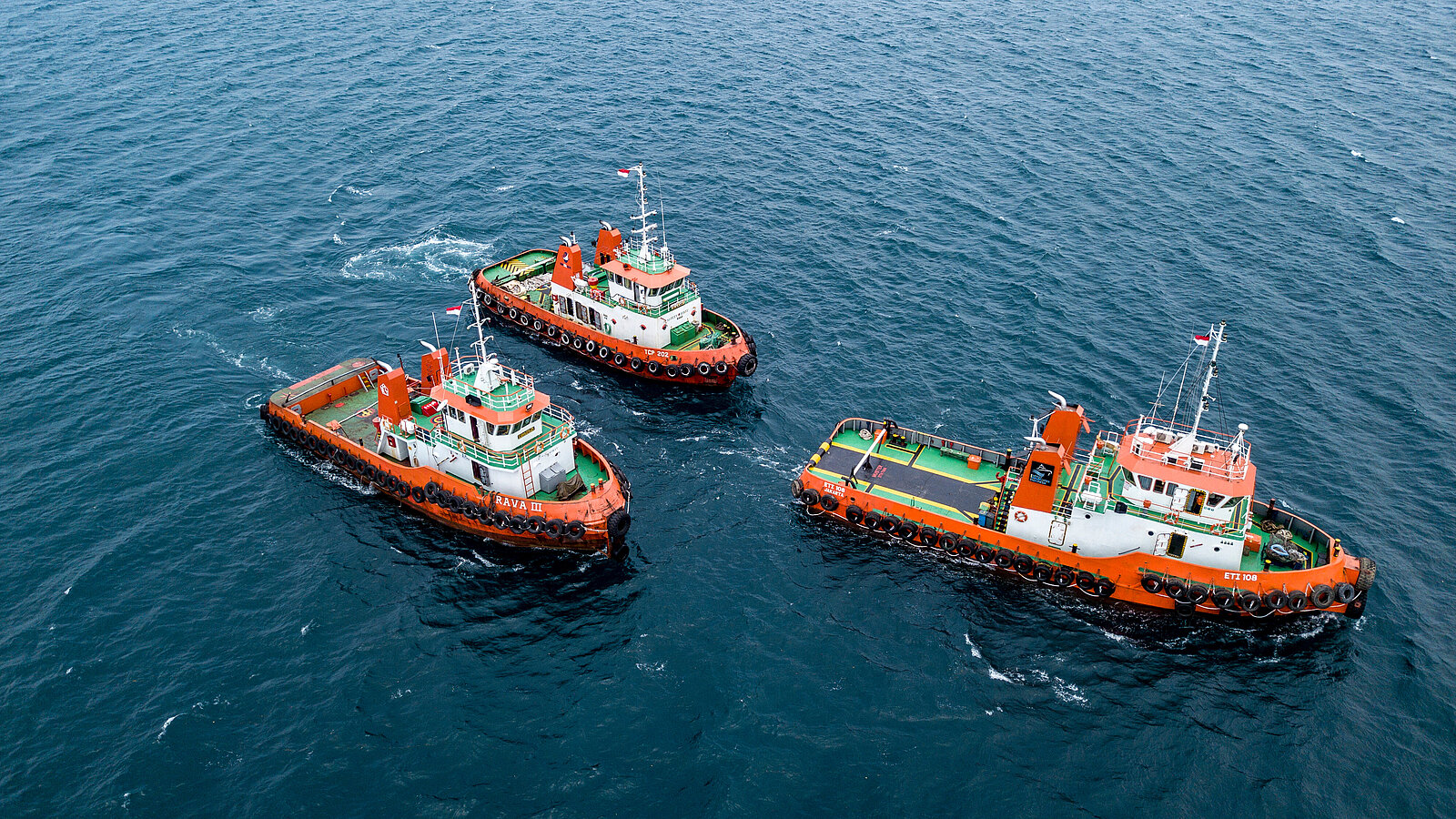 Drei orange-weiße Boote auf ruhigem Wasser, eines leicht voraus