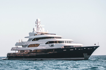 Eine große weiße Yacht mit mehreren Decks fährt auf dem Meer. Der Himmel ist klar und hell.